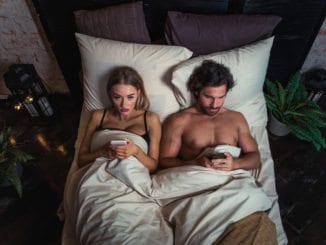 couple in bed on cellphones looking unhappy