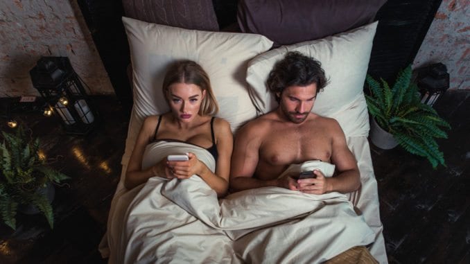 couple in bed on cellphones looking unhappy
